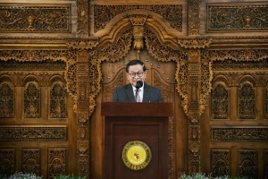 "Pejabat Pemprov DKI Jakarta berbicara di podium dalam acara resmi, dengan latar belakang ukiran kayu tradisional Indonesia di Kedutaan Besar Republik Indonesia di Seoul."