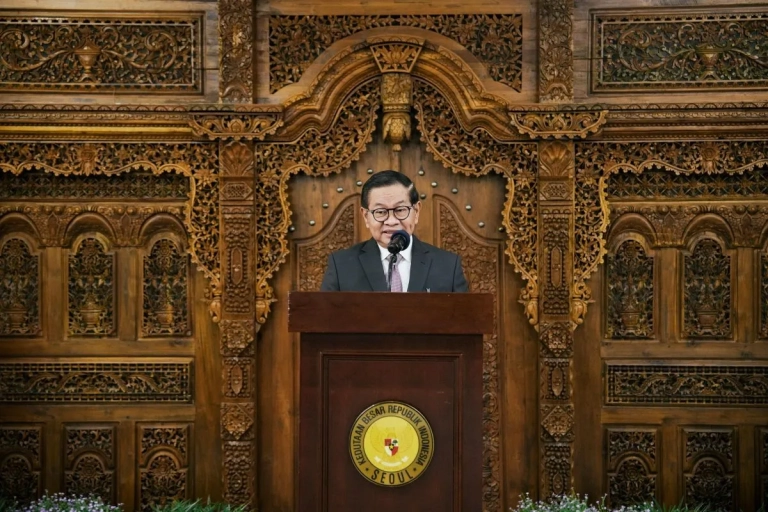 "Pejabat Pemprov DKI Jakarta berbicara di podium dalam acara resmi, dengan latar belakang ukiran kayu tradisional Indonesia di Kedutaan Besar Republik Indonesia di Seoul."