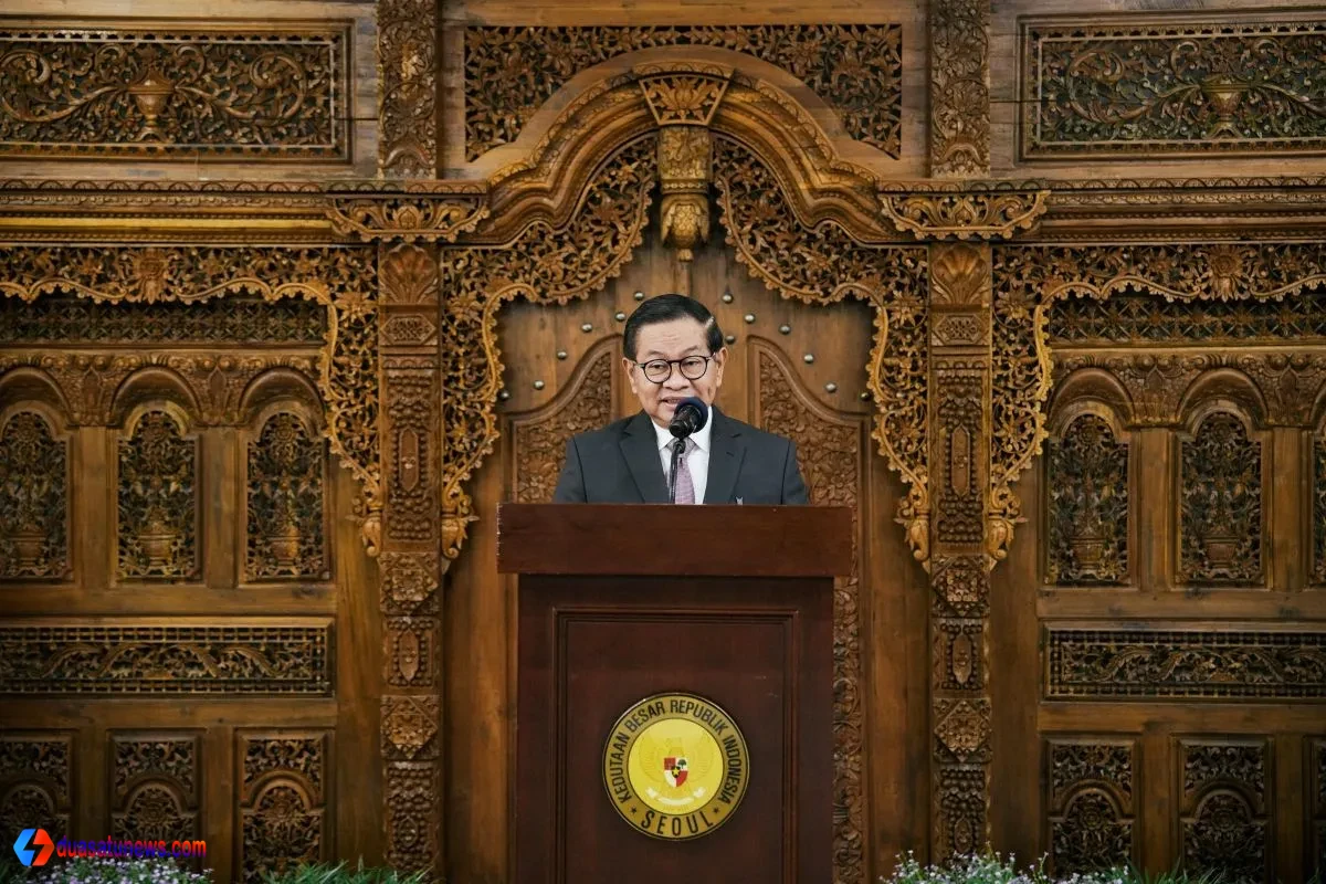 "Pejabat Pemprov DKI Jakarta berbicara di podium dalam acara resmi, dengan latar belakang ukiran kayu tradisional Indonesia di Kedutaan Besar Republik Indonesia di Seoul."